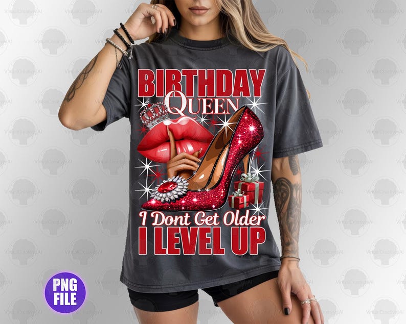 May include: Dark gray t-shirt with a graphic design featuring the text "BIRTHDAY QUEEN" and "I DON'T GET OLDER I LEVEL UP". The design includes a red high heel, red lips, a crown, and a gift box.