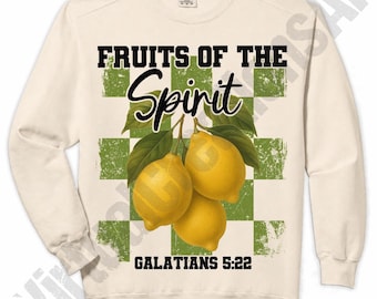 May include: Cream-colored sweatshirt with the text "FRUITS OF THE Spirit" and "GALATIANS 5:22". The design features three yellow lemons with green leaves against a green and white checkered background.