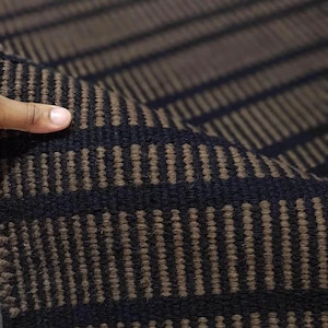 May include: A woven textile featuring a repeating pattern of thick black horizontal stripes alternating with textured brown bands composed of small, vertical, raised rectangular segments. The fabric has a dense, durable, and tactile construction.