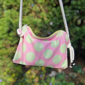Può includere: Una borsa a tracolla in tessuto a pois rosa e verde con una tracolla in corda bianca e una chiusura a zip.