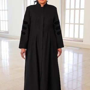 May include: A floor-length black robe featuring a high mandarin collar, a concealed front button placket, and long sleeves adorned with three horizontal velvet-textured bands on each forearm. The garment has a structured fit with subtle pleats.