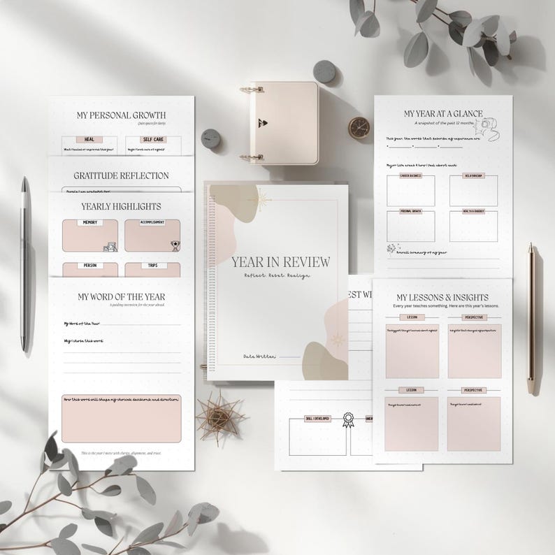 May include: A neutral-toned planner and journal set, ideal for reflection. The planner, titled "Year in Review", features pages for personal growth, yearly highlights, and insights. Two pens and decorative items are also visible in the image.
