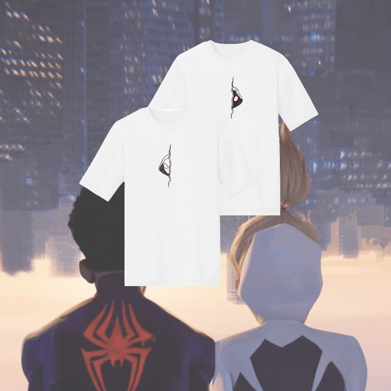 Pode incluir: Duas camisetas brancas com um gr&aacute;fico de olho preto e rosa impresso na frente. As camisetas s&atilde;o mostradas em duas pessoas em p&eacute; em frente a um horizonte da cidade.