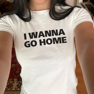 Puede incluir: Camiseta blanca con texto negro que dice "I wanna go home".