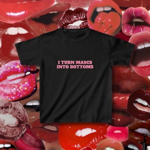 May include: Black t-shirt with pink text that reads "I turn mascs into bottoms".