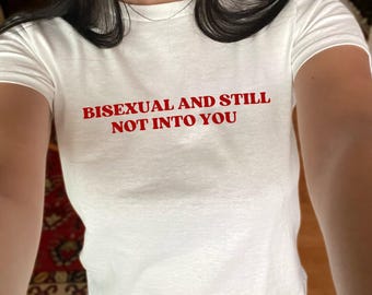 Puede incluir: Camiseta blanca con texto rojo que dice "Bisexual y aún no me interesas."