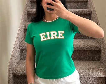 May include: Green short-sleeved t-shirt with the word "EIRE" in white and orange letters. The model is wearing a size XS.