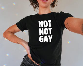 以下が含まれることがあります： 白地に「NOT NOT GAY」とプリントされた黒いTシャツです。