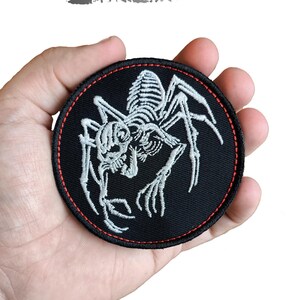 Op de afbeelding: Een zwarte, ronde geborduurde patch met een wit spinnen skelet ontwerp en een rode rand. De patch heeft de tekst "DIGITAL EMBROIDERY DESIGN" bovenaan en "Instant Download" onderaan.