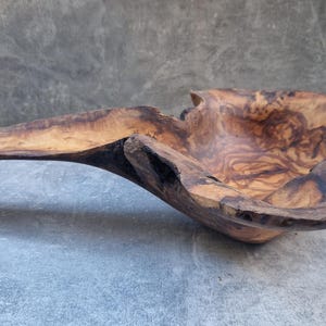 Könnte beinhalten: Eine handgefertigte Holzschale mit einer einzigartigen, organischen Form. Die Schale besteht aus hellbraunem Holz mit dunkelbraunen und schwarzen Akzenten. Die Schale hat eine lange, gebogene Verlängerung auf einer Seite.