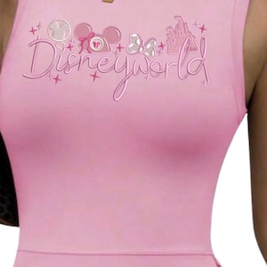May include: Pale pink sleeveless bodysuit featuring the text "Disneyworld". The design includes Mickey Mouse ears, a bow, and a castle. The bodysuit is a solid pink colour.