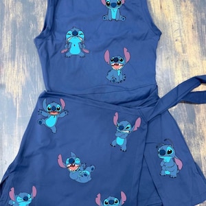 May include: A sleeveless navy blue dress featuring a wrap-style skirt with a tie closure. The fabric is printed with multiple small, colourful illustrations of the character Stitch in various poses, including sitting, laughing, and standing.