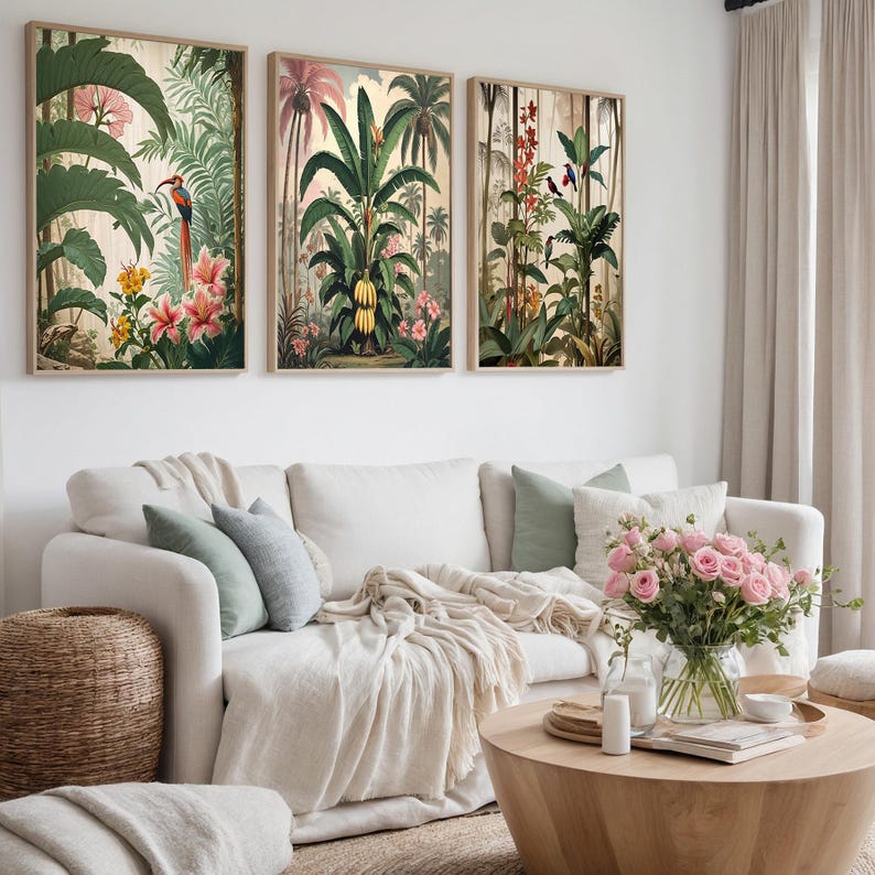 Three framed botanical prints showcasing tropical plants, flowers, and birds. The artwork has a vintage style with warm colours, displayed above a white sofa with decorative cushions. The prints are in wooden frames.