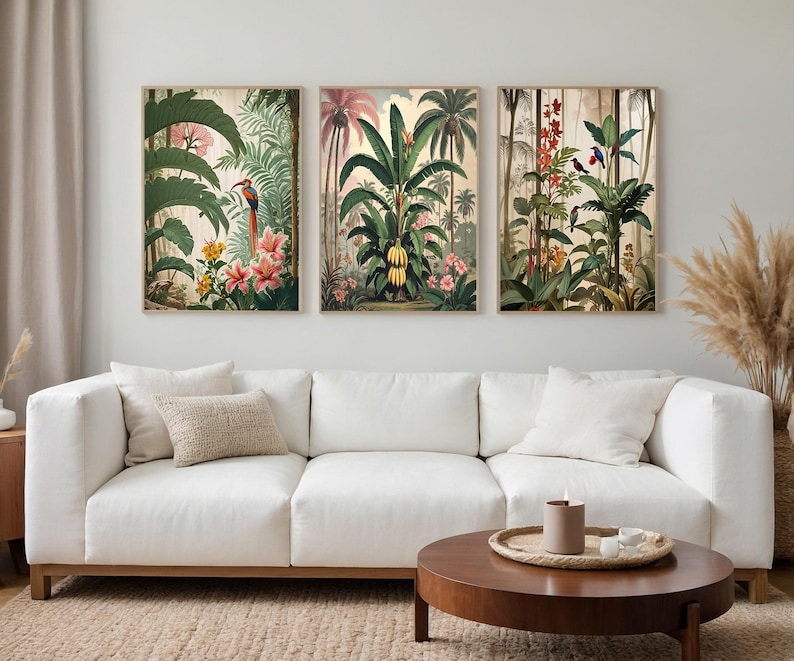 Three framed botanical prints depicting tropical scenes with plants and birds. The artwork features vibrant green foliage, pink and yellow flowers, and various birds. The prints are displayed above a white sofa in a living room.