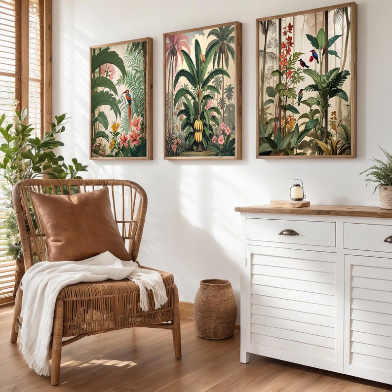 Three framed botanical prints depicting tropical scenes hang above a white cabinet. A wicker chair with a brown leather cushion and a white throw sits in front of a window with wooden blinds. A decorative vase is on the floor.