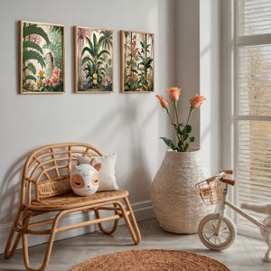 Three framed botanical prints with gold frames hang on a light grey wall. A rattan bench with a decorative animal head pillow sits below the prints. A large white vase with peach roses and a small white bicycle are also in the room.