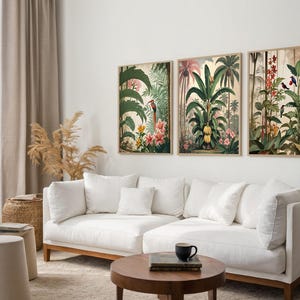 Three framed botanical prints depicting tropical scenes with palm trees, flowers, and birds. The artwork has a vintage style with a warm colour palette. The prints are displayed above a white sectional sofa in a living room setting.