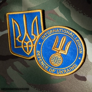 Könnte beinhalten: Zwei gestickte Aufnäher, einer mit dem ukrainischen Wappen und der andere mit dem Text "Internationale Legion Verteidigung der Ukraine" und einem stilisierten Dreizack.