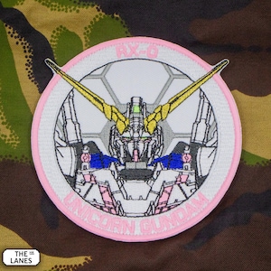 Puede incluir: Parche bordado rosa y blanco con una cabeza de robot blanca en el centro. El robot tiene una antena amarilla y una placa de pecho azul y blanca. El texto "RX-78" está por encima del robot y "GUNDAM" está por debajo del robot.