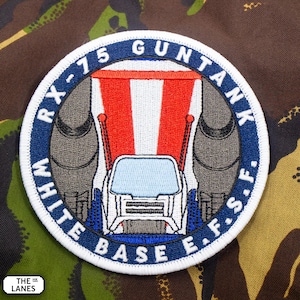 May include: A circular embroidered patch featuring a Guntank robot design with red, white, and blue colours. The text RX-75 GUNTANK and WHITE BASE E.F.S. is stitched in white within a dark blue border. The patch has a white outer edge.