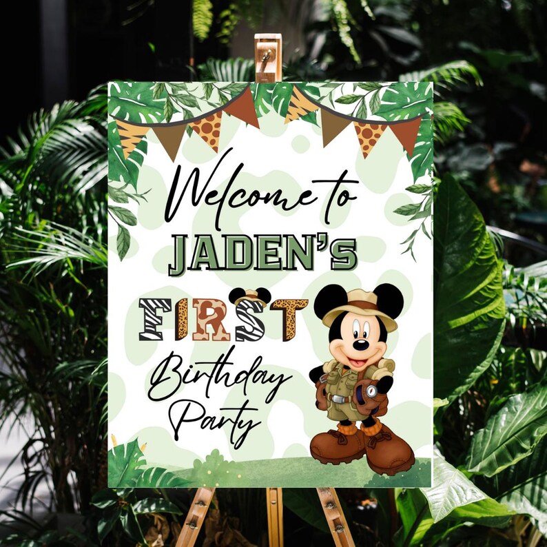 May include: Welcome to Jaden's First Birthday Party sign with a jungle theme. The sign features a cartoon Mickey Mouse dressed as an explorer with a green background and a leafy border.