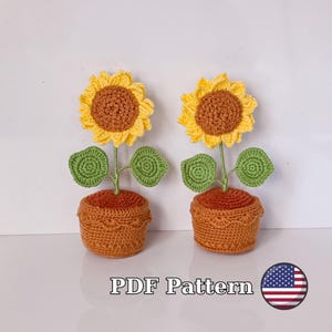 May include: Two crocheted sunflower plants in orange pots. The sunflowers have yellow petals and brown centres. The plants have green leaves. The image includes the text "PDF Pattern" and a small American flag.