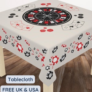 May include: A square casino-themed tablecloth. The off-white cloth is decorated with a roulette wheel, playing cards, and poker chips in red, black, and white. The tablecloth is on a wooden table.