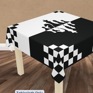 May include: A square tablecloth featuring a black and white checkered border pattern. The center displays a split design with a white half and a black half, decorated with a symmetrical graphic of chess pieces. The text Tablecloth Only is visible.