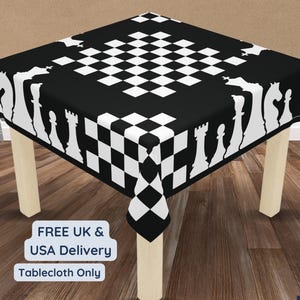 Puede incluir: Un mantel negro y blanco con temática de ajedrez sobre una mesa pequeña. El mantel presenta un patrón de cuadros en el centro y siluetas de piezas de ajedrez blancas en los bordes. El texto "Tablecloth Only" es visible.