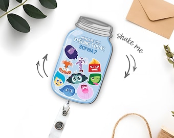 May include: A light blue mason jar-shaped badge reel featuring the text "HOW ARE YOU FEELING TODAY, SOPHIA?" and various colorful cartoon character faces. The design includes a clear plastic strap with a metal clip at the bottom for attachment.