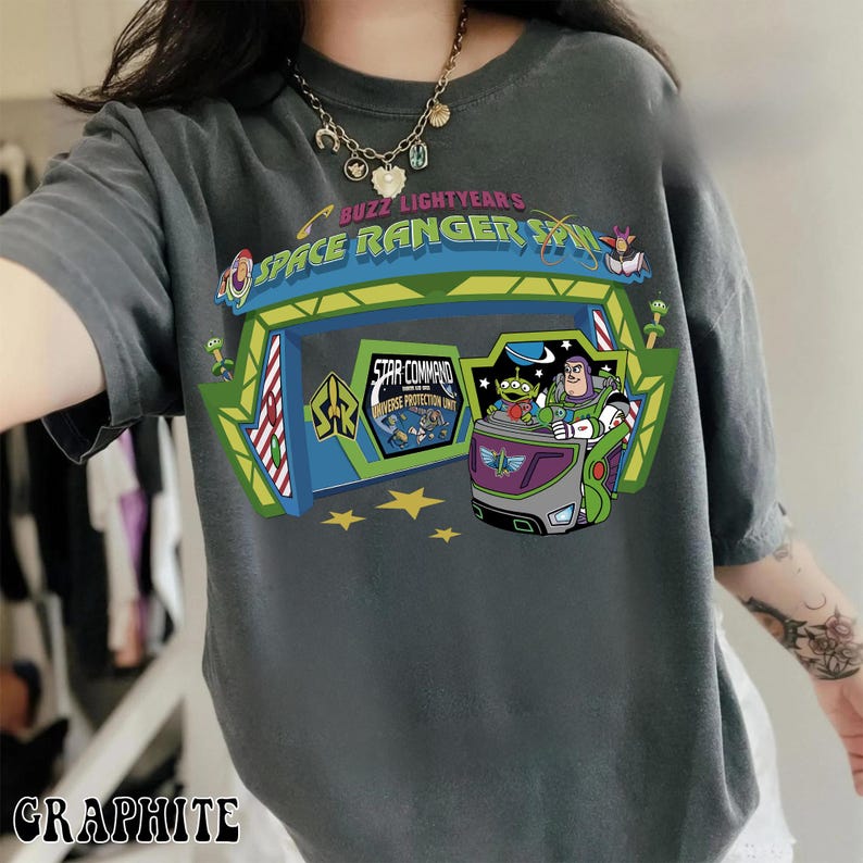 K&ouml;nnte beinhalten: Graphitfarbenes T-Shirt mit einer farbenfrohen Grafik von Buzz Lightyear und den Aliens aus Toy Story in einem Space Ranger Spin-Fahrzeug. Das Shirt tr&auml;gt den Text "BUZZ LIGHTYEARS SPACE RANGER SPIN".