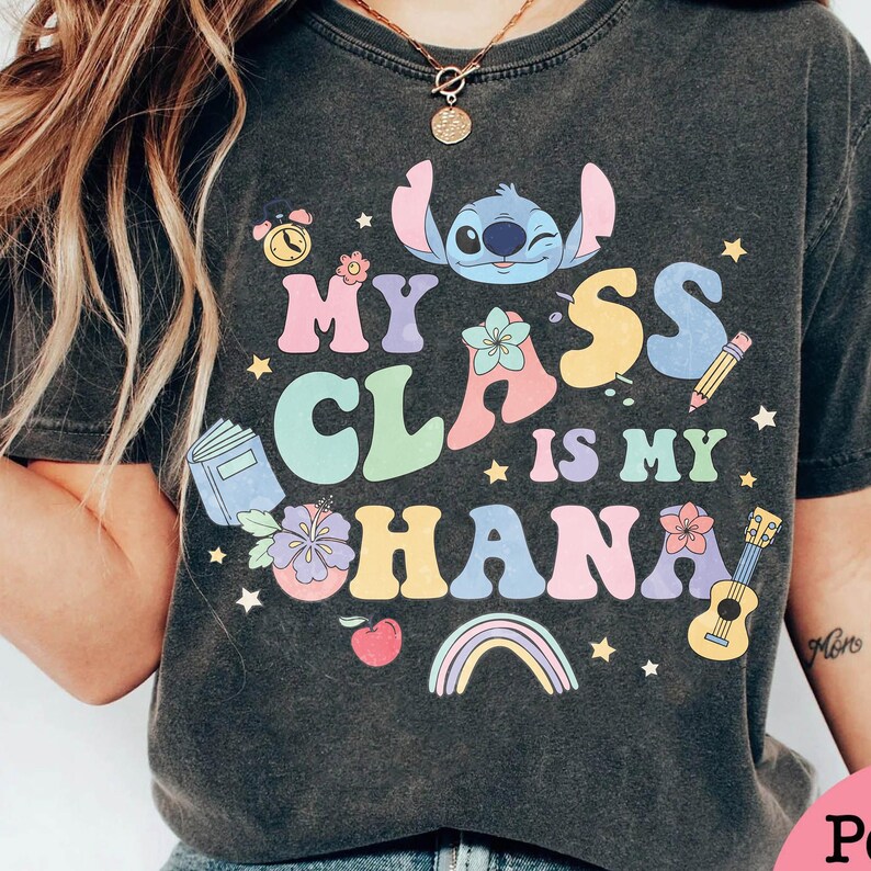Puede incluir: Camiseta gris oscuro con un gr&aacute;fico colorido que dice "My Class is My Ohana", con un personaje de dibujos animados, flores, un arco&iacute;ris y un ukelele. La camiseta tiene un aspecto vintage y desgastado.