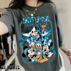 May include: Graphite-colored t-shirt featuring a graphic of Disney characters, including Mickey, Minnie, Donald, Daisy, Goofy, and Pluto. The design includes the text "MOTUNUI NATIONAL PARK" in a blue and white tropical theme.
