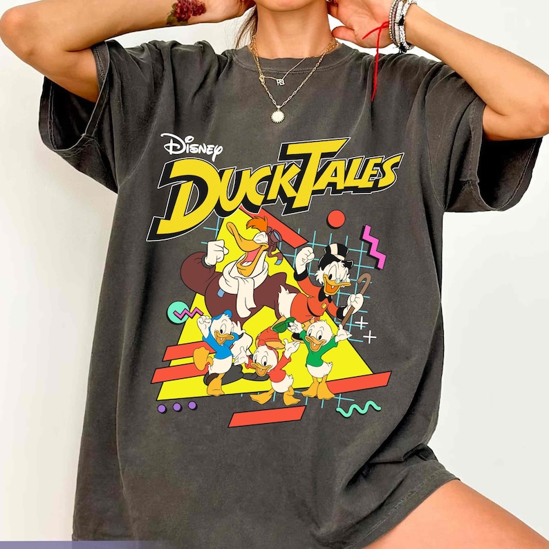 May include: A gray t-shirt with a vintage-style graphic of the Disney DuckTales characters. The graphic features Scrooge McDuck, Huey, Dewey, Louie, and Launchpad McQuack. The text "Disney DuckTales" is printed in yellow and red.