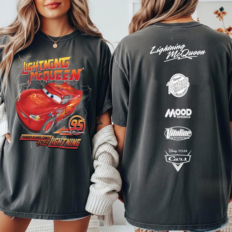 May include: Dark gray t-shirt featuring Lightning McQueen from the Disney Pixar Cars movie. The front graphic shows the red race car with the text "Lightning McQueen" and "95". The back of the shirt displays the text "Lightning McQueen" and other logos.
