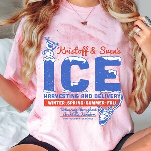 May include: A pink tie-dye t-shirt with a blue and white graphic of Olaf and Sven. The graphic says "Kristoff & Sven's ICE HARVESTING AND DELIVERY WINTER; SPRING SUMMER FALL Delivering throughout Arendelle Kingdom CONTACT SVEN FOR DETAILS".