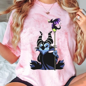 May include: A pink tie-dye t-shirt with a cartoon image of Stitch dressed as Maleficent from Disney's Sleeping Beauty. Stitch is holding a staff with a purple dragon on top.