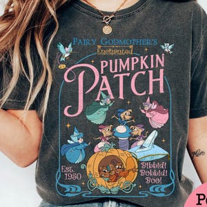 May include: Dark gray t-shirt featuring a whimsical design with the text "Fairy Godmother's Enchanted Pumpkin Patch." The graphic includes illustrations of fairy godmothers, mice, a pumpkin carriage, and Cinderella's glass slipper. The shirt also has the text "Bibbidi Bobbidi Boo!" and "Est. 1950."