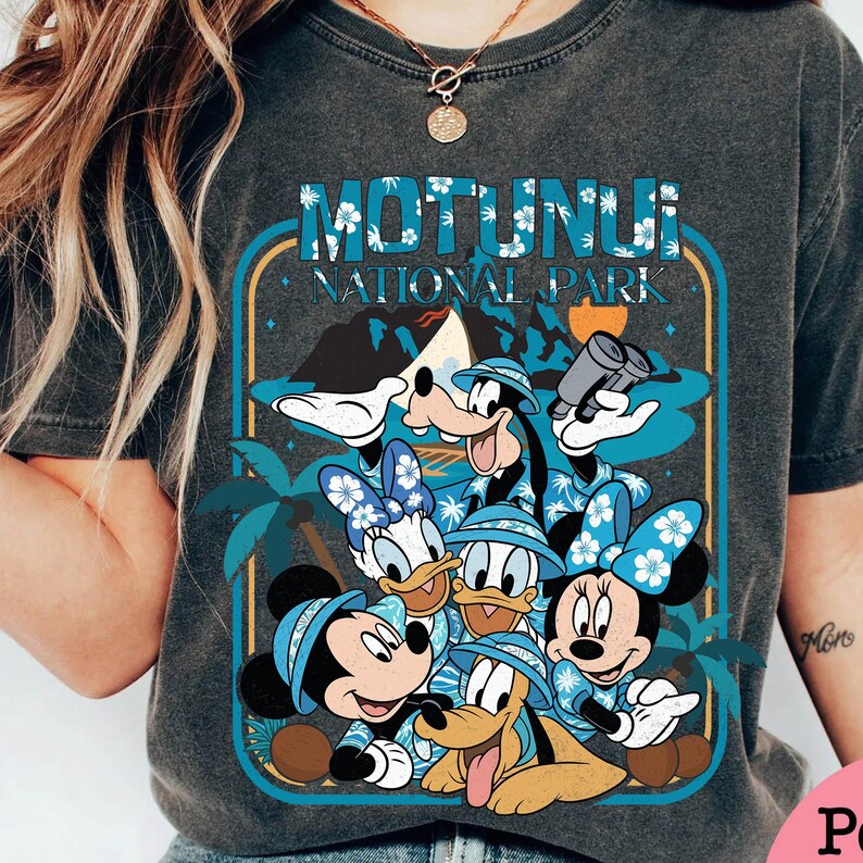 May include: Dark gray t-shirt featuring a graphic of Disney characters, including Mickey, Minnie, Donald, Daisy, Goofy, and Pluto, in Hawaiian shirts and hats. The design includes the text "MOTUNUI NATIONAL PARK" in a blue and white font, with palm trees and a mountain in the background.