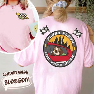 May include: Light pink t-shirt with a cartoon sloth design. The front features a small graphic with a sloth and the word "FLASH". The back has a larger design with the words "FLASH 100 YARD DASH" around a sloth in a car.