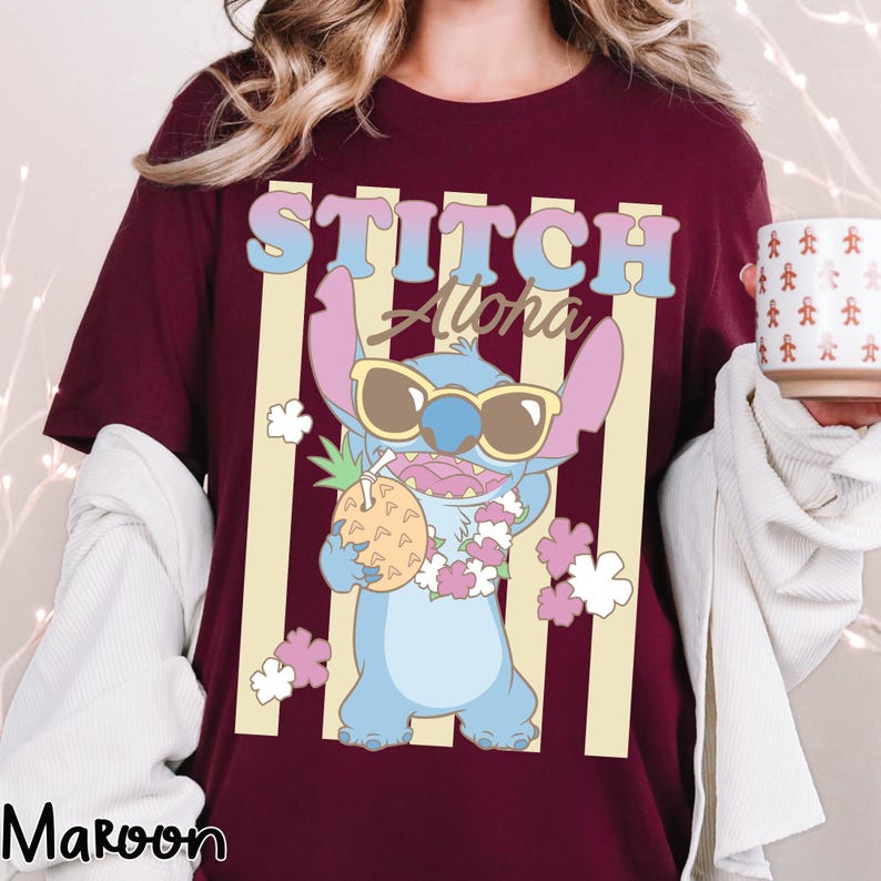 K&ouml;nnte beinhalten: Burgunderfarbenes T-Shirt mit einer Cartoon-Figur von Stitch, die eine Sonnenbrille tr&auml;gt und eine Ananas h&auml;lt. Der Text "STITCH Aloha" befindet sich &uuml;ber der Figur, mit vertikalen gelben Streifen im Hintergrund. Das Wort "Maroon" steht unten.