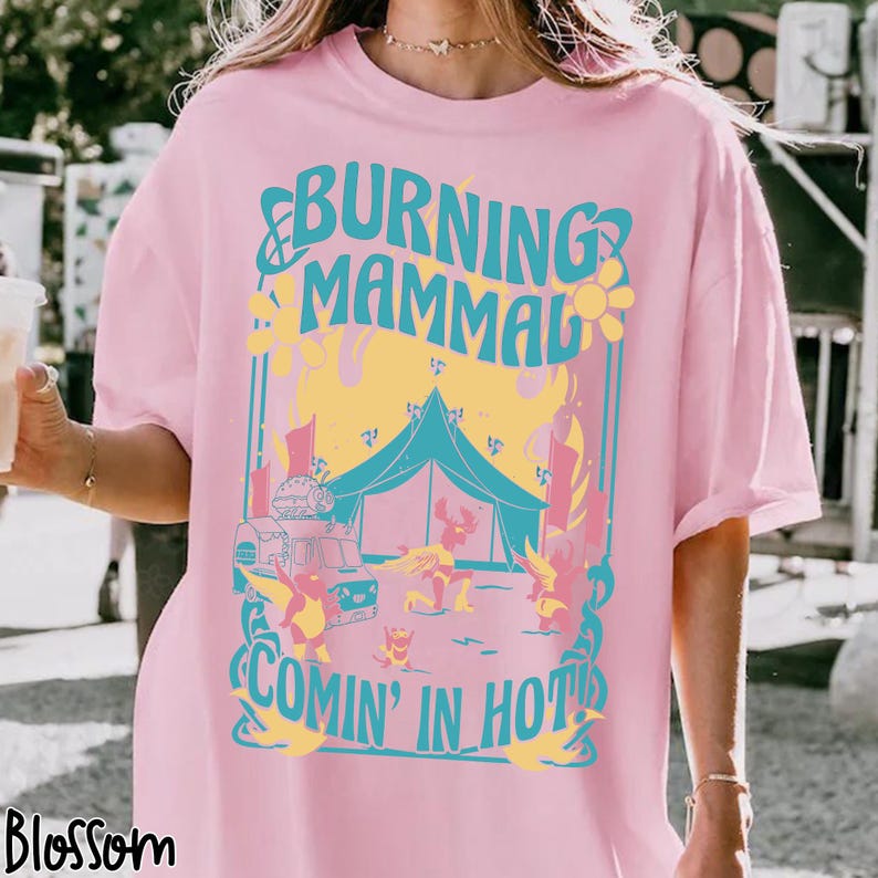 Puede incluir: Camiseta rosa claro con un dise&ntilde;o gr&aacute;fico turquesa y amarillo. El dise&ntilde;o presenta el texto "BURNING MAMMAL COMIN' IN HOT!", una tienda de campa&ntilde;a, un cami&oacute;n de comida y figuras de dibujos animados.
