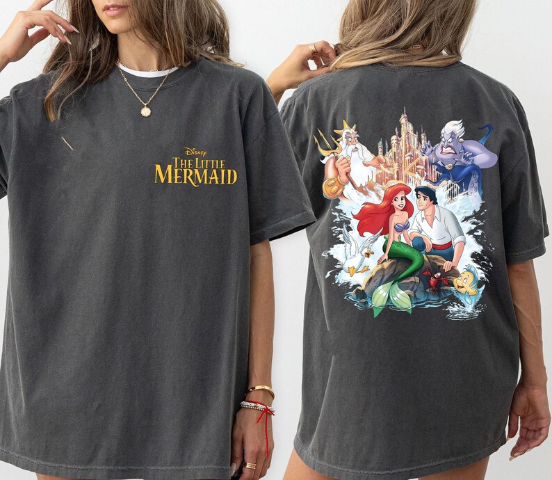 May include: A dark gray t-shirt with a graphic print of Ariel, Prince Eric, and Ursula from Disney's The Little Mermaid. The text "Disney The Little Mermaid" is printed on the front of the shirt.