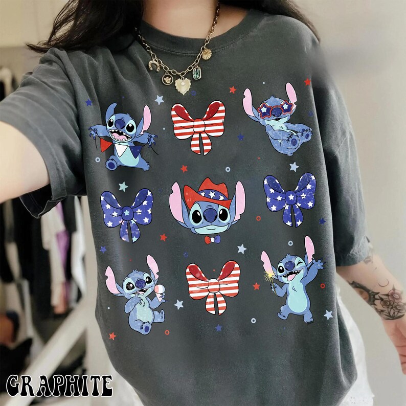 May include: Graphite-coloured t-shirt with a design of cartoon Stitch characters in various poses, alongside patriotic bow ties and accessories. The design includes red, white, and blue stars and bow tie graphics.