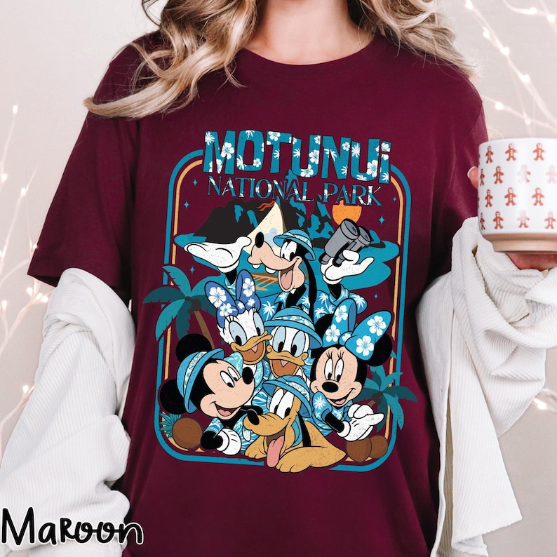 May include: Maroon t-shirt featuring a graphic of Disney characters, including Mickey, Minnie, Donald, Daisy, Goofy, and Pluto, with the text "Motunui National Park." The characters are wearing Hawaiian shirts and hats. The design is framed in a teal and blue border.