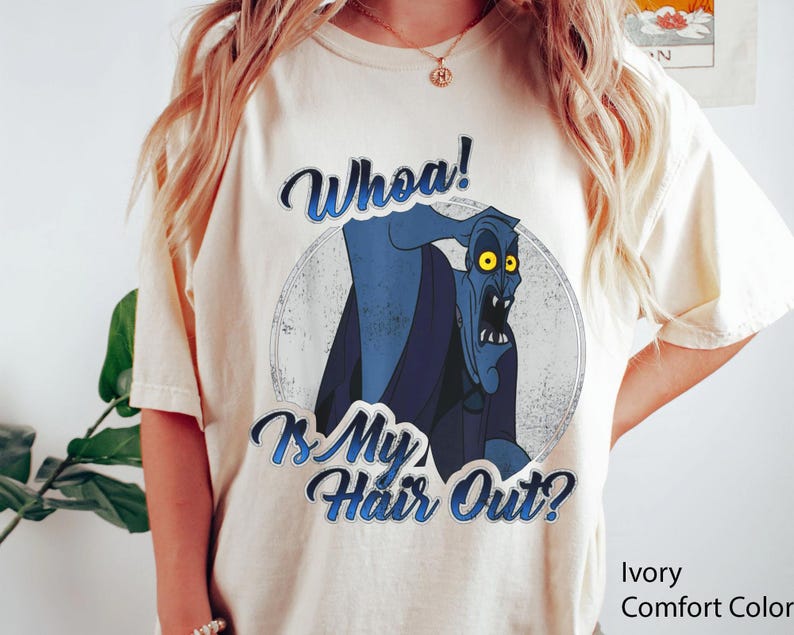 Puede incluir: Camiseta de color marfil con un gr&aacute;fico desgastado de un personaje de dibujos animados azul con ojos amarillos. El texto "Whoa! Is My Hair Out?" est&aacute; impreso encima y debajo del personaje en una fuente azul. La camiseta es de la marca Comfort Color.