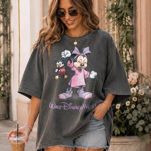 May include: Dark gray oversized t-shirt featuring Mickey and Minnie Mouse. Minnie is wearing a pink dress and bow. Mickey is in red shorts. The text "Walt Disney World" is printed below the characters.