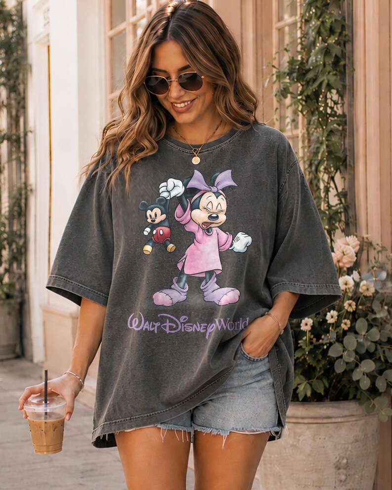 May include: Dark gray oversized t-shirt featuring Mickey and Minnie Mouse. Minnie is wearing a pink dress and bow. Mickey is in red shorts. The text "Walt Disney World" is printed below the characters.
