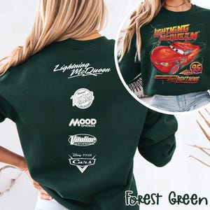 May include: Forest green sweatshirt featuring Lightning McQueen from the Disney Pixar Cars movie. The front displays a graphic of the red race car with the text "Lightning McQueen". The back has the text "Lightning McQueen" and other logos.