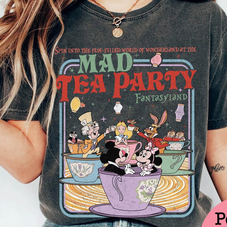 Puede incluir: Camiseta gris oscuro con un gr&aacute;fico colorido de la Mad Tea Party de Fantasyland de Disney. El dise&ntilde;o incluye personajes como el Sombrerero Loco, Alicia y Mickey y Minnie Mouse en tazas de t&eacute;. El texto dice "MAD TEA PARTY" y "FANTASYLAND".